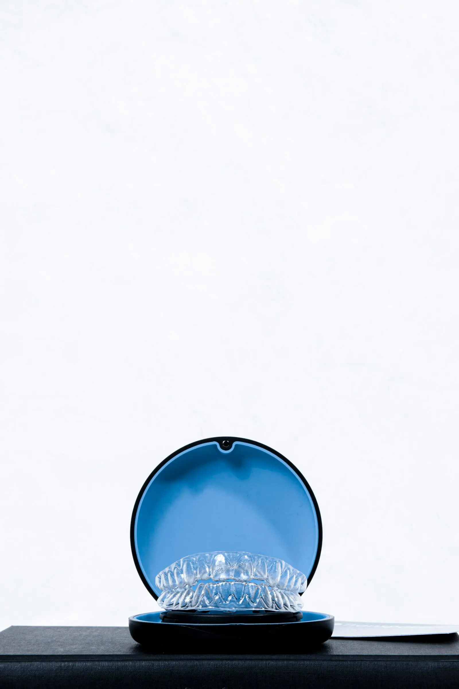 Clear aligners in an open round blue case on a black box against white