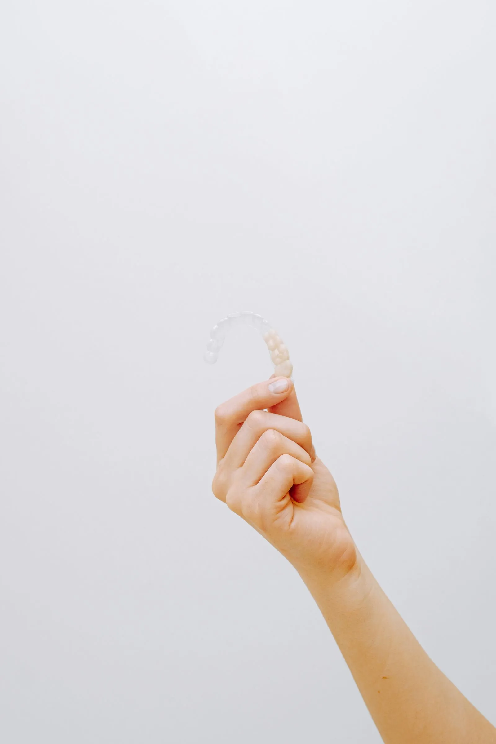 Hand holding a clear plastic aligner against a plain white background