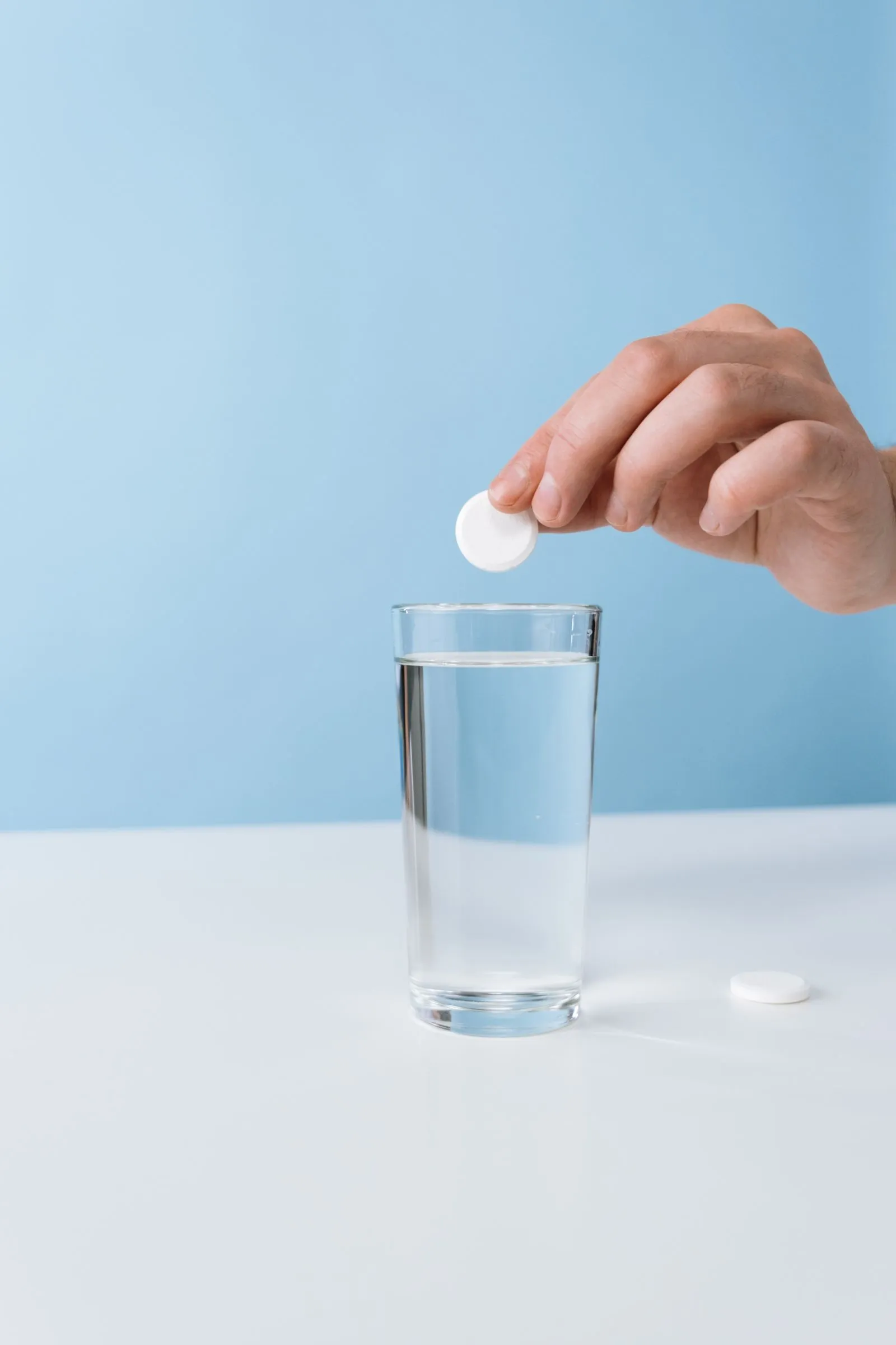 Hand dropping an effervescent tablet into a glass of water on light blue