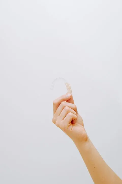 Hand holding a clear plastic aligner against a plain white background